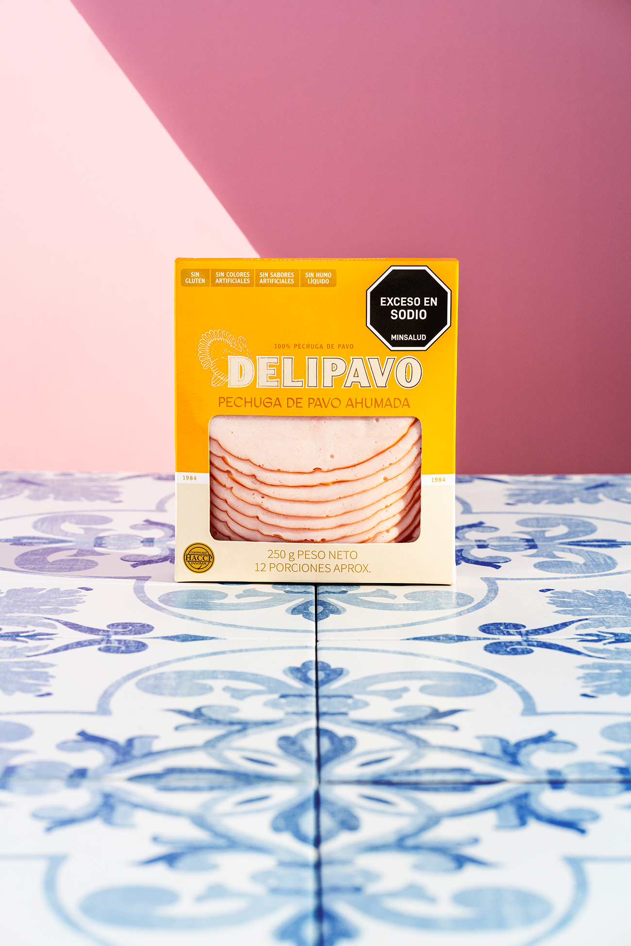 Empaque de Pechuga de Pavo Ahumada Delipavo sobre superficie azul con fondo rosa.